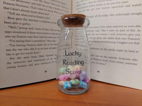 corked jar labeled lucky reading stars with lucky stars inside in front of open book