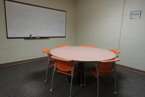 Conference room with a round table with 6 chairs around it. There is a white board mounted on the wall.