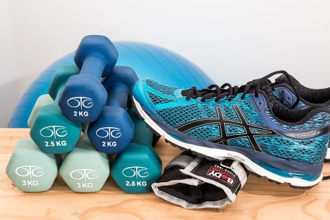 Six hand weights, one ankle weight and two tennis shoes on a wooden bench in front of an exercise ball.