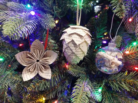 three ornaments made using recycled book pages hanging in a lit Christmas tree