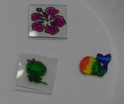 Three Shrinky Dinks with a purple flower, green dinosaur with a purple bow and a rainbow-colored whale.