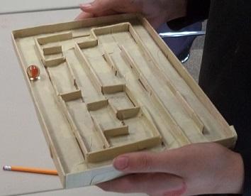 Image of a person holding a marble maze made from cardboard and masking tape with a marble in the maze.