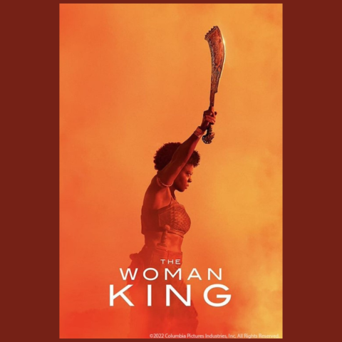 The movie poster for "The Woman King" that has the image of a woman facing the right holding up a decorated hatchet. She is wearing a short top, skirt, a knife on the side of the skirt and bracelets on her wrist and upper arm.