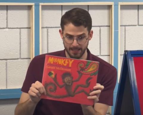Man wearing glasses and a maroon polo shirt holding the book "Monkey" with the cover towards the audience.