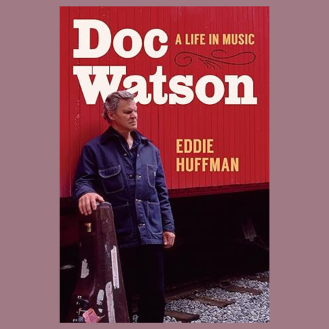 Cover of "Doc Watson: A Life in Music" that has a man with a guitar case propped up beside him standing in front of a red train car with tracks showing underneath.