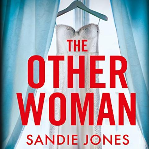 The cover of "The Other Woman" by Sandie Jones. It features a wedding dress hanging on a hanger in front of a window with sheer blue curtains drawn to the sides, allowing light to filter through. The title, THE OTHER WOMAN, is prominently displayed in bold, uppercase red letters in the center, with the author's name, SANDIE JONES, written below it in smaller red text.