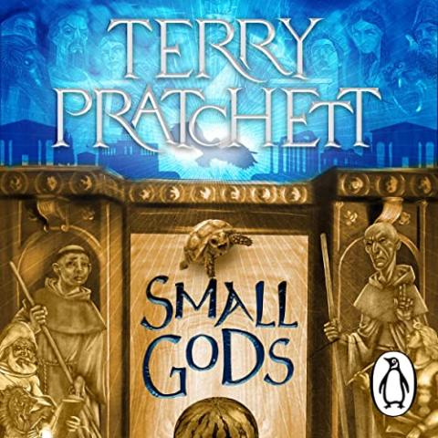 Cover of Small Gods by Terry Pratchett. The top half features the author’s name in large, white capital letters against a glowing blue background with ghostly, ethereal faces of figures looking down. Below, in the center, the title “Small Gods” is written in bold, stylized letters. The background is golden, with two carved panels showing robed, monk-like figures; one holds a book, while the other holds a staff. Above the title, a small turtle with an inquisitive expression is depicted.