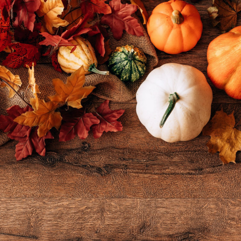 Picture of multi-color pumpkins and autumn leaves with burlap on a wooden surface.