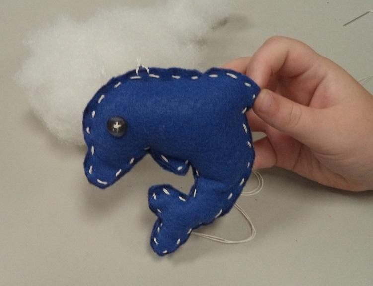 A hand holding a blue felt dolphin with white stitching around the edges.